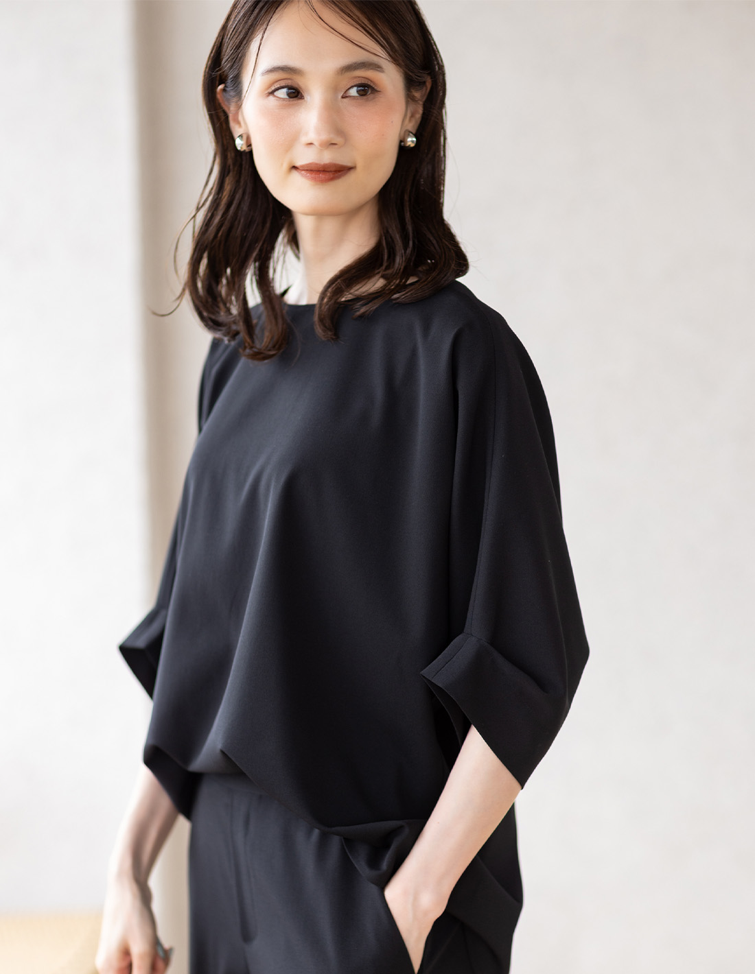 ブラックのストレッチシャーリングドルマンブラウス・ブラックのストレッチストレートパンツを着用した女性--1