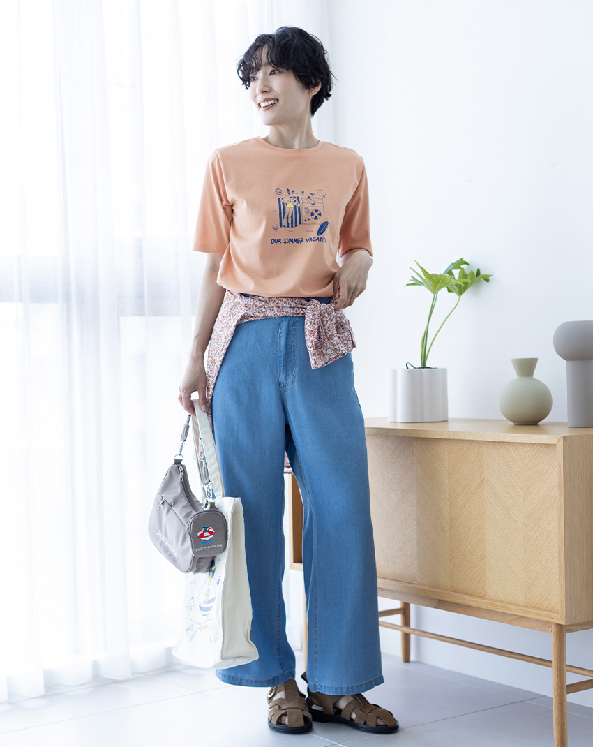 サーモンピンクの【ひやさらコットン トムさんコラボ】コイくんプリントTシャツ・ブルーのデニムストレートパンツ・ピンクのコットンジョーゼット総柄プリントブラウス・【トムさんコラボ】コイくんワンポイント刺しゅうポーチ付きショルダーバッグ

を着用した女性--1