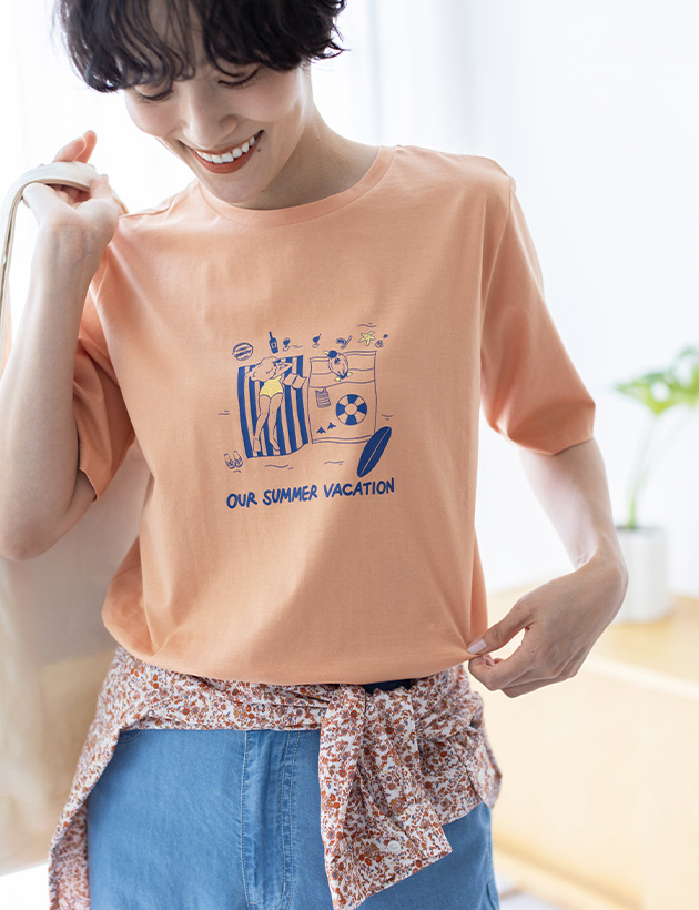 サーモンピンクの【ひやさらコットン トムさんコラボ】コイくんプリントTシャツ・ブルーのデニムストレートパンツ・ピンクのコットンジョーゼット総柄プリントブラウス・【トムさんコラボ】コイくんワンポイント刺しゅうポーチ付きショルダーバッグ

を着用した女性--2