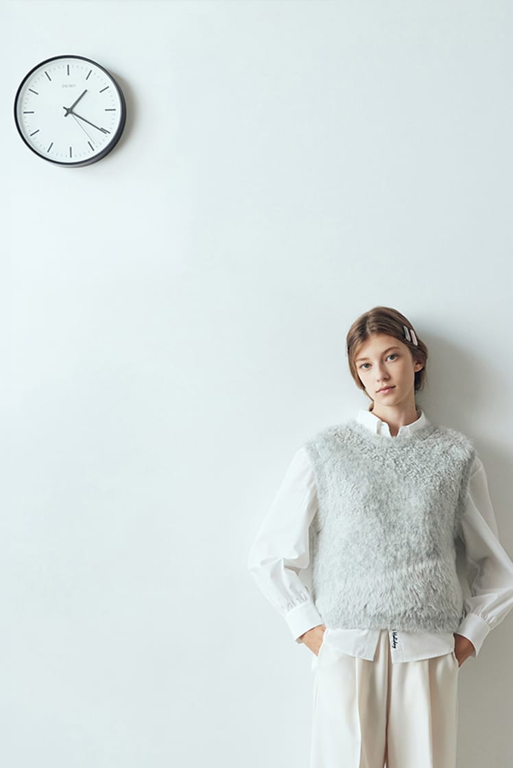 白のモヘアベストと白シャツ、白パンツのコーディネート（時計のある室内）